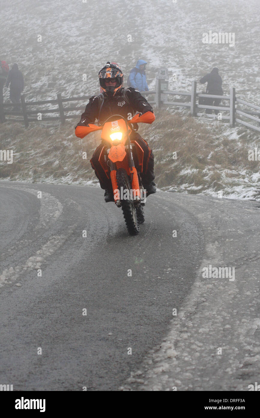 A motorcyclist tackles mist and snowy road conditions on a bend in Castleton, Peak District, Derbyshire, UK Stock Photo