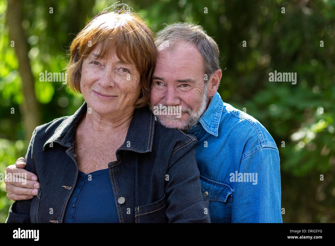 Old couple outside in a park with trees behind them Stock Photo