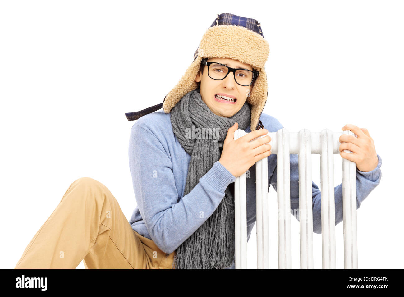 Chilled young man with winter hat sitting next to a radiator Stock Photo