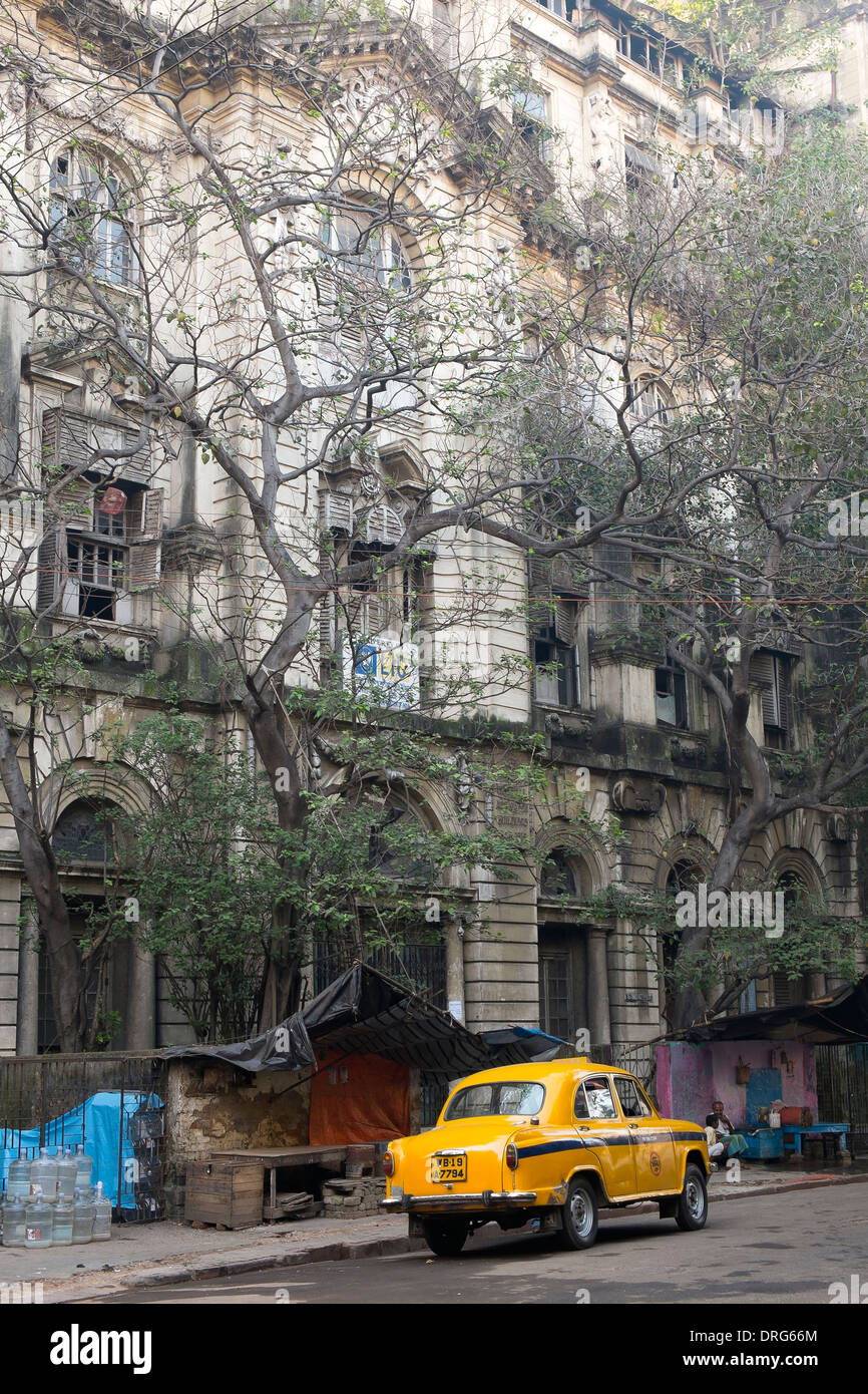 India, West Bengal, Kolkata, yellow Ambassador taxi parked outside dilapidated colonial style building Stock Photo