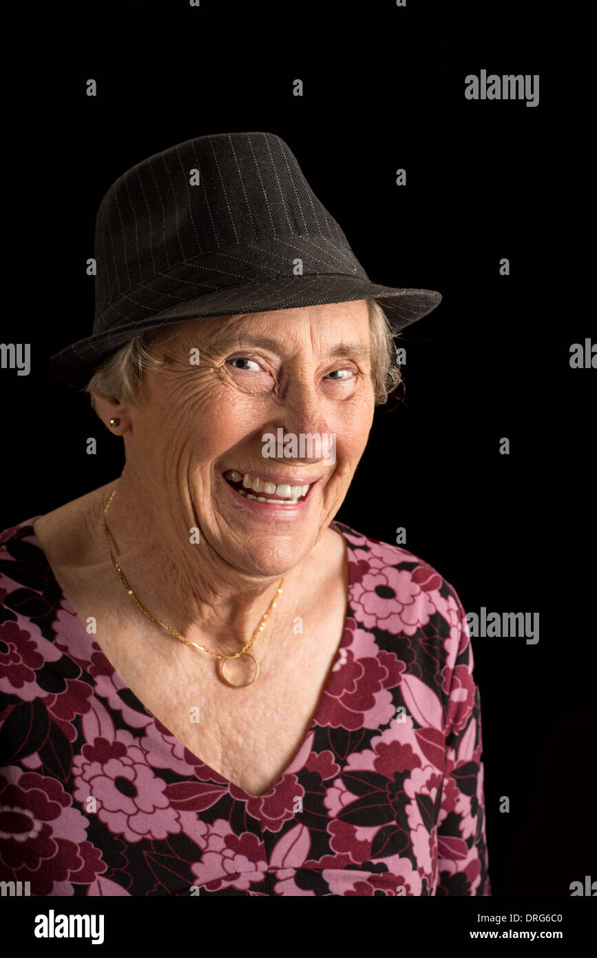 Senior lady wearing a fedora laughing isolated on black Stock Photo