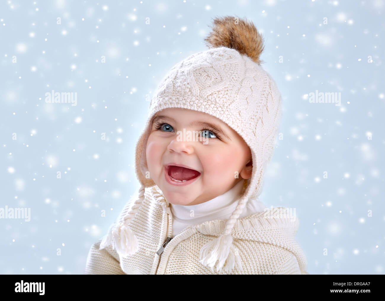 Portrait of cute little baby girl wearing warm stylish hat isolated on blue snowy background, snow falling, winter season Stock Photo
