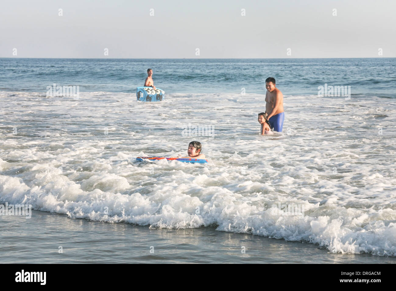 young Mexican boy completes good ride on boogie board as a dad with daughter watch with smiling approval San Agustinillo Mexico Stock Photo