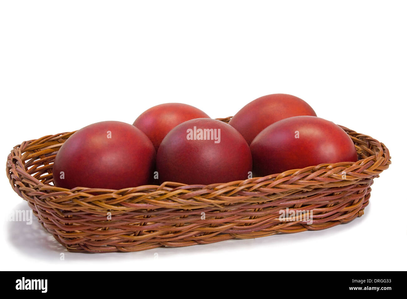 Three Easter eggs, painted in red, are beautifully decorated with wicker basket. Presented on a white background. Stock Photo