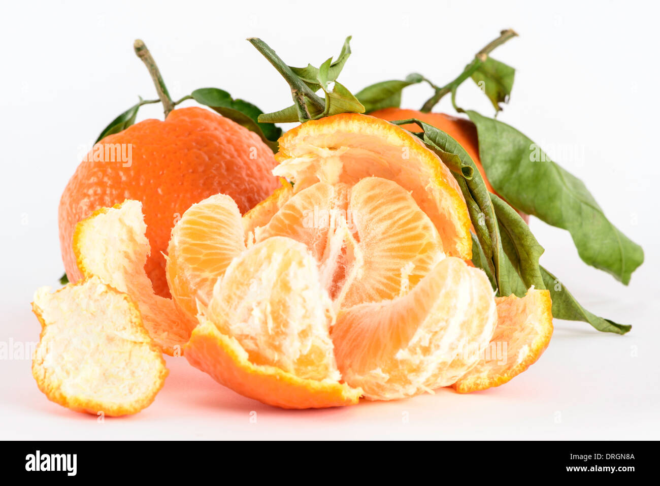 Three Satsumas with stalks and leaves, one opened with segments broken