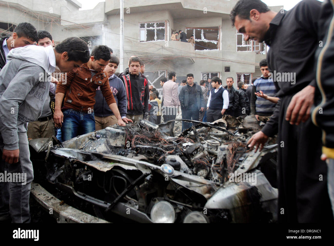 Kirkuk, Iraq. 26th Jan, 2014. People gather around a damaged vehicle at the blast site in Kirkuk, Iraq, on Jan. 26, 2014. At least four people were killed and 14 wounded in the afternoon when three car bombs detonated almost simultaneously in separate neighborhoods in the city of Kirkuk, some 250 km north of the Iraqi capital of Baghdad, a local police source told Xinhua on condition of anonymity. Credit:  Dena Assad/Xinhua/Alamy Live News Stock Photo