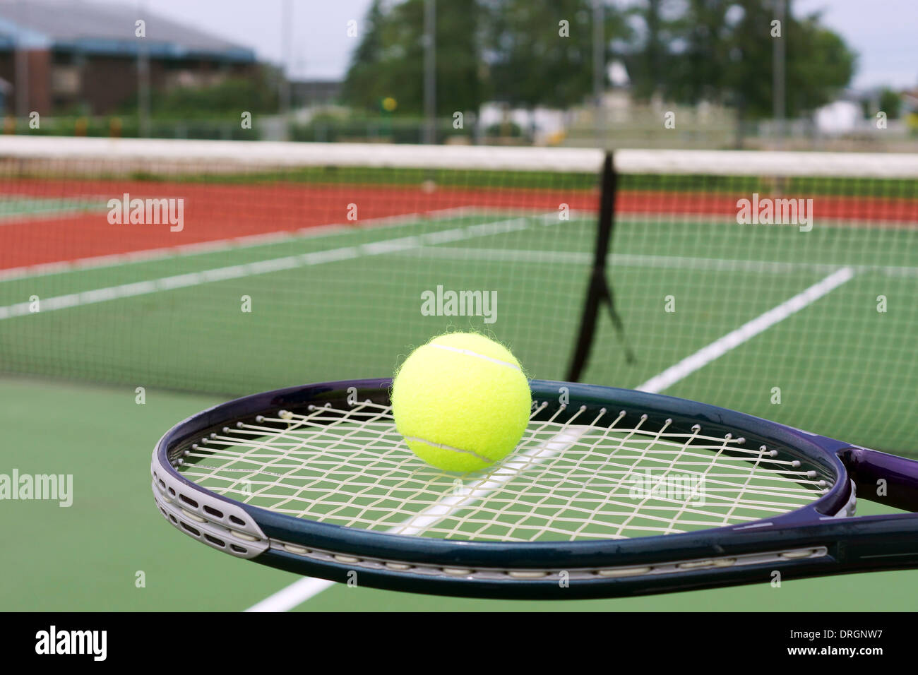 Tennis concept, ball on racket in front of net on hard court Stock Photo