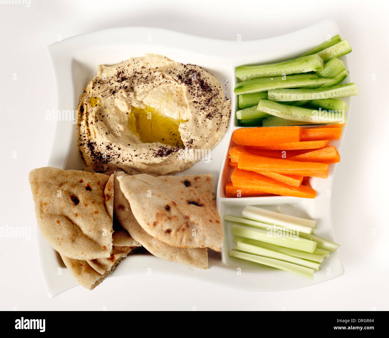 Top view of a dip tray with hummus, bread, carrot sticks, celery and cucumber. Stock Photo