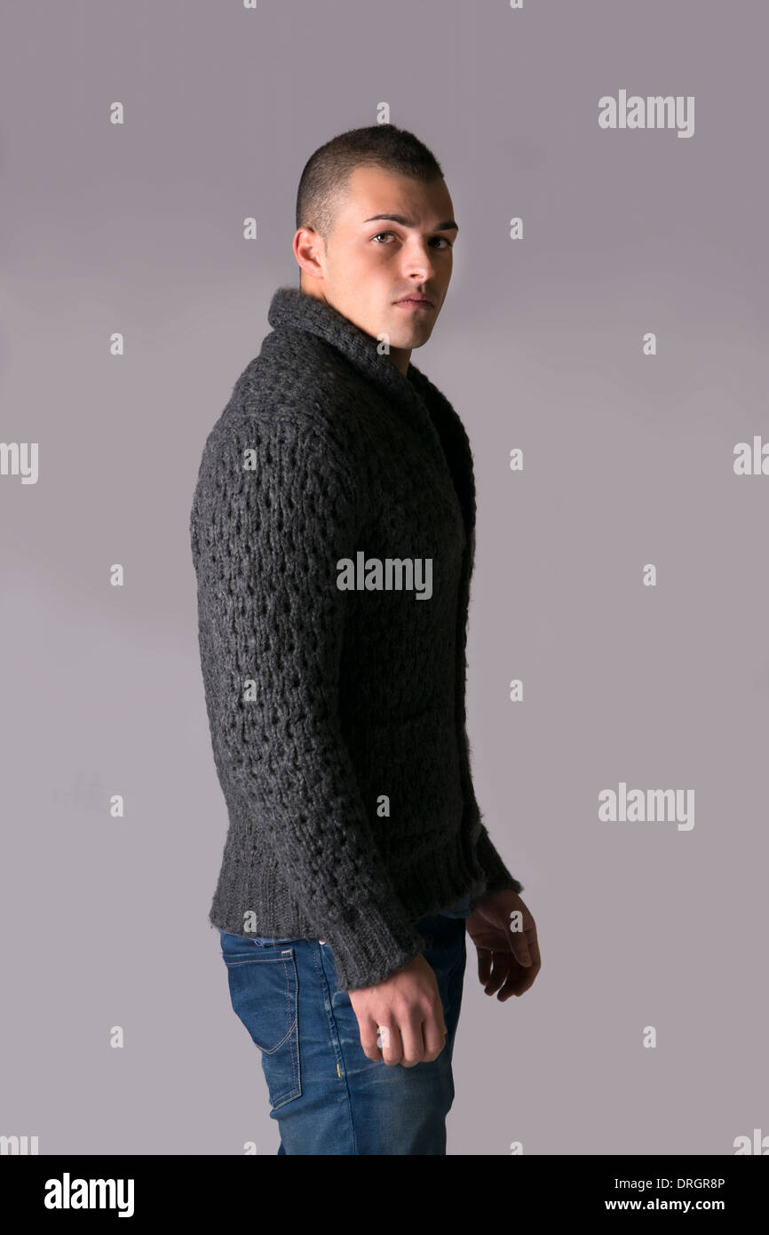Attractive young man with wool sweater and jeans, isolated on grey background Stock Photo