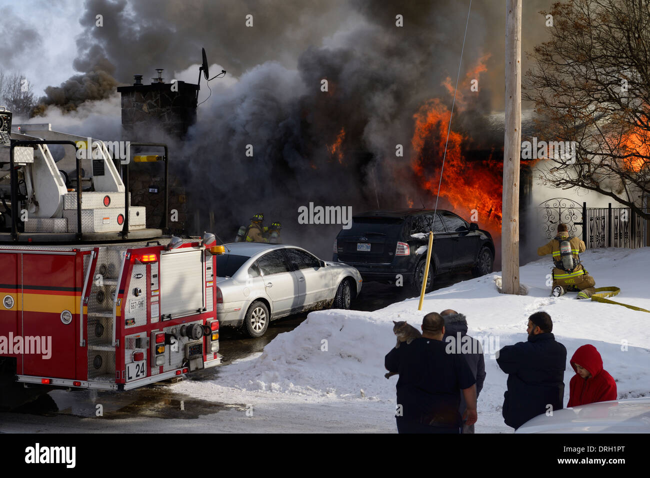 Family outside in winter watching while house goes up in flames with firefighters spraying water to knock down the blazing structural fire Ottawa Stock Photo