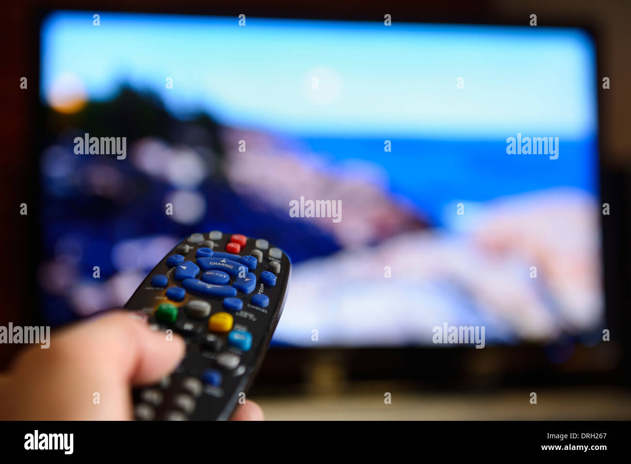 Person pointing a universal remote control towards a television screen entertainment system Stock Photo