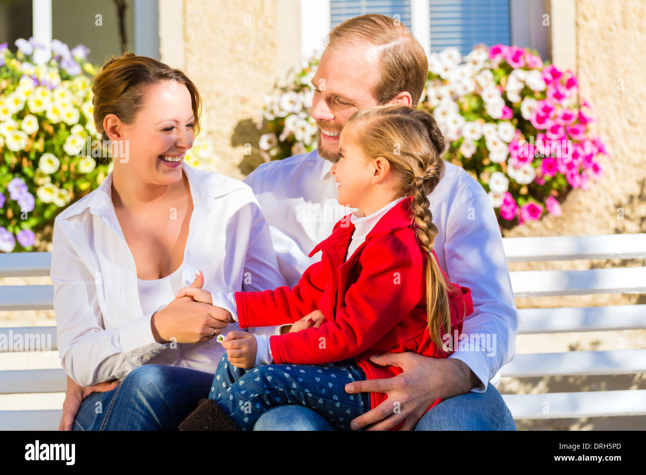 Family with mother, father and daughter together on garden bench in front of home Stock Photo