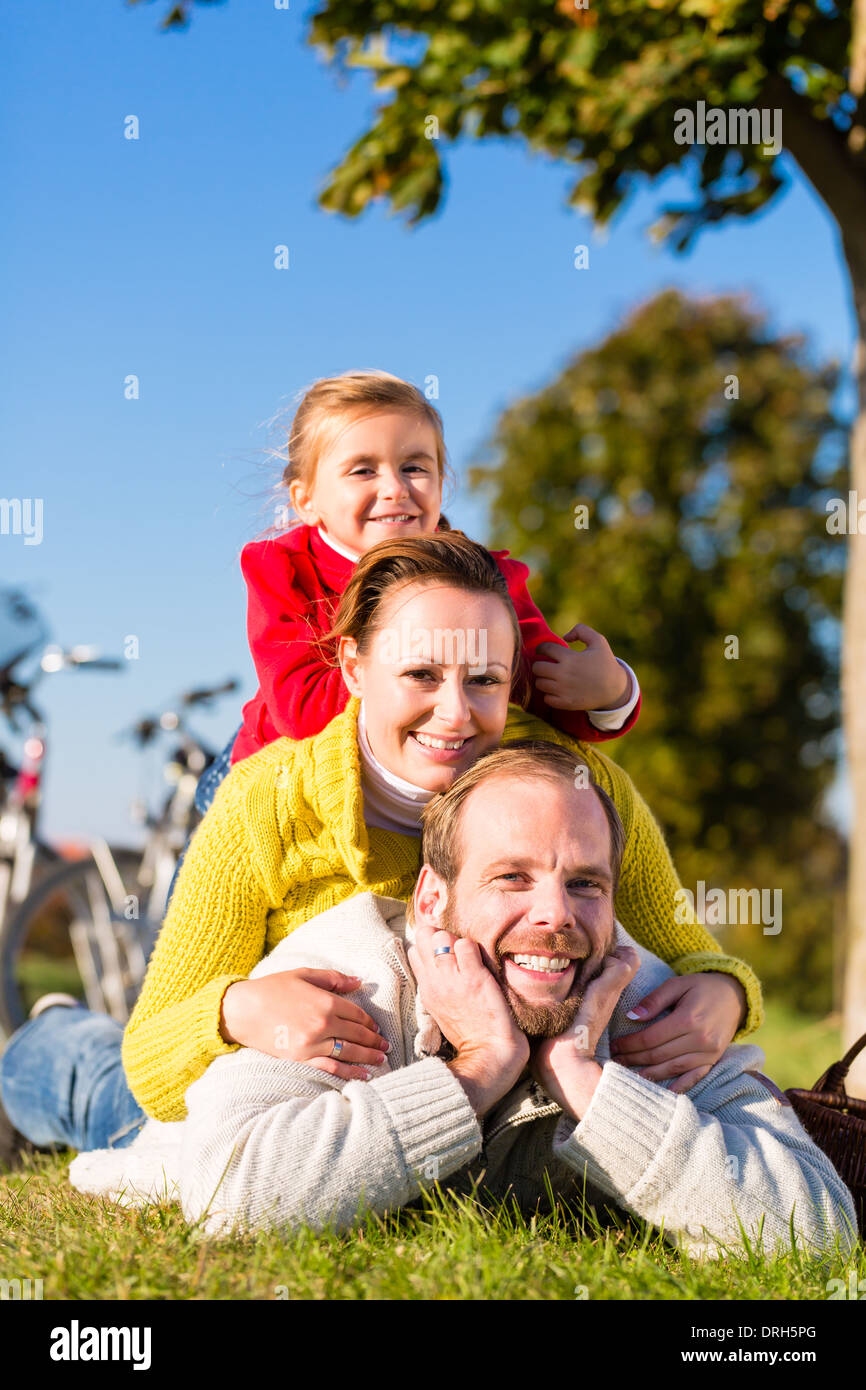 Family with mother, father and daughter having break on family trip with bicycle or cycle in park Stock Photo