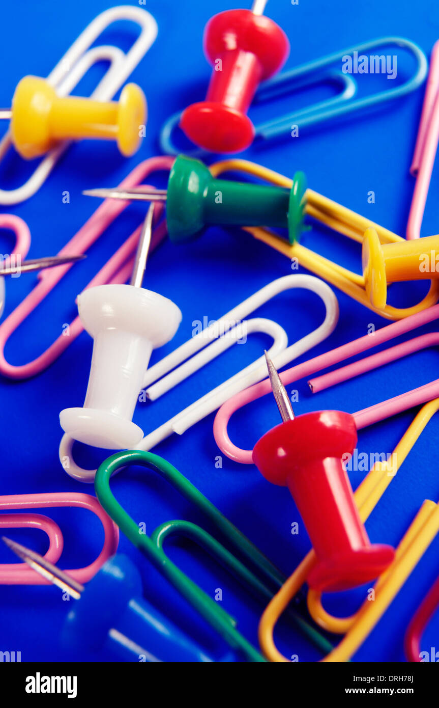 Colorful thumbtacks and paperclips on blue background, office supplies conceptual still life Stock Photo