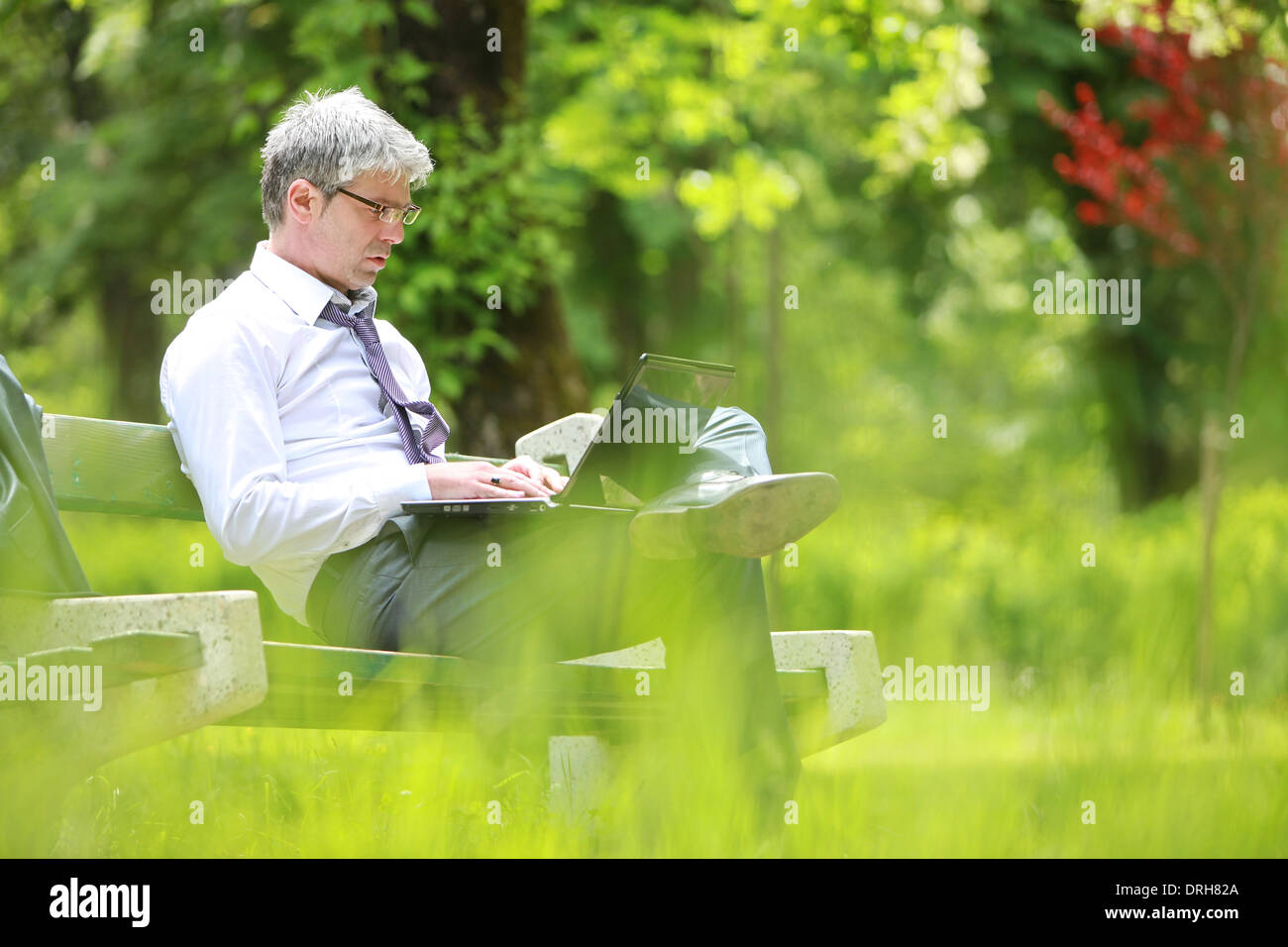 A young handsome businessman using laptop sitting on a bench in a park ...