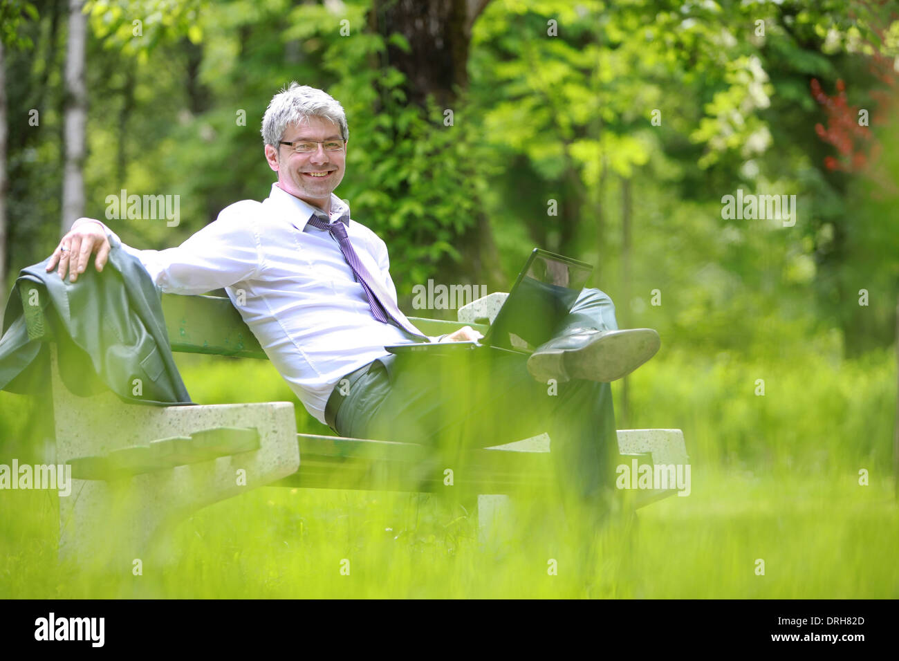 A young handsome businessman using laptop sitting on a bench in a park ...