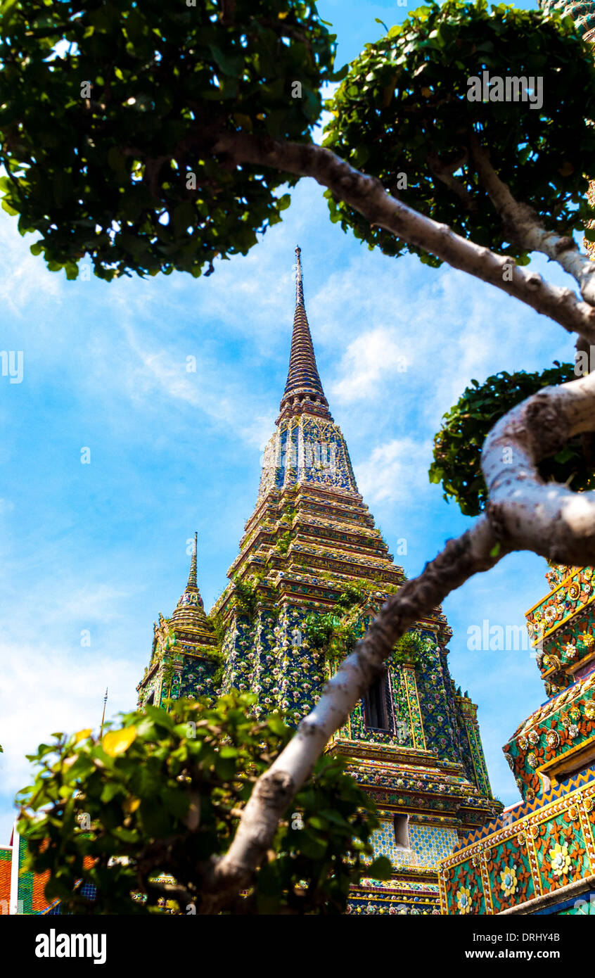 Ornate colourful, ceramic exterior of Wat Pho Temple of Reclining Buddha, framed by a bonsai tree. Bangkok. Stock Photo