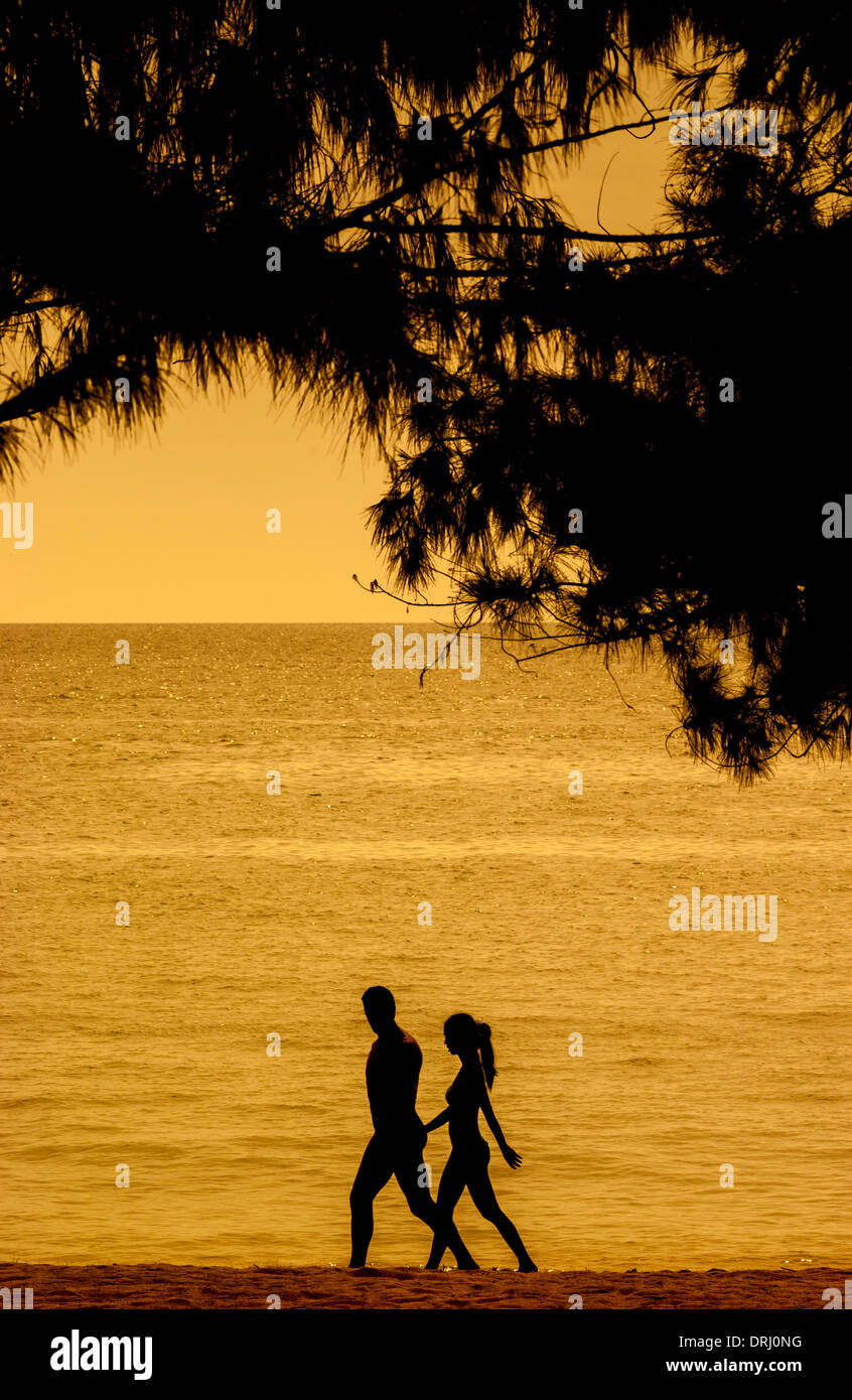 Silhouetted couple, holding hands whilst walking along a beach at ...