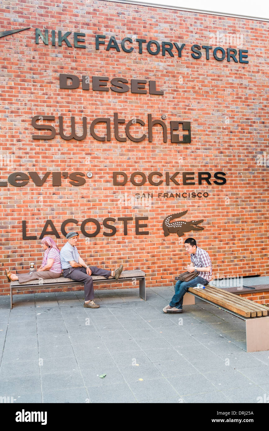 exhausted shoppers in front of a brick wall with fashion brand logos, outlet city, metzingen, baden-wuerttemberg, germany Stock Photo
