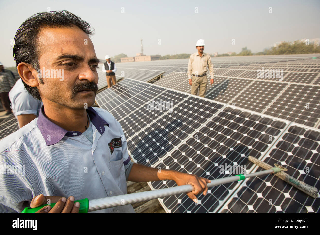 Workers washing the dust off solar panels at a 1 MW solar power station run by Tata power on the roof of an electricity company Stock Photo