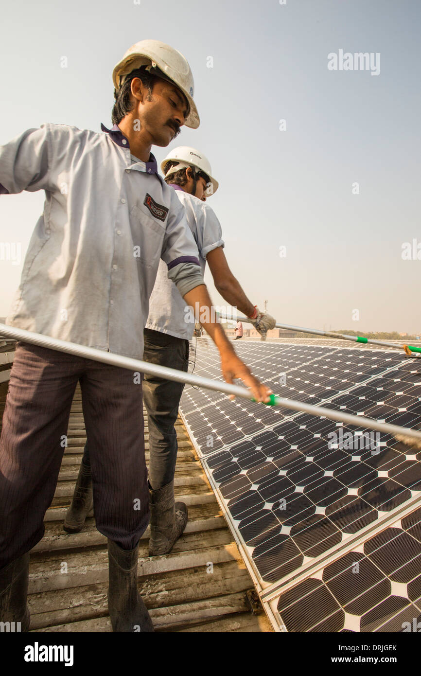 Workers washing the dust off solar panels at a 1 MW solar power station run by Tata power on the roof of an electricity company Stock Photo