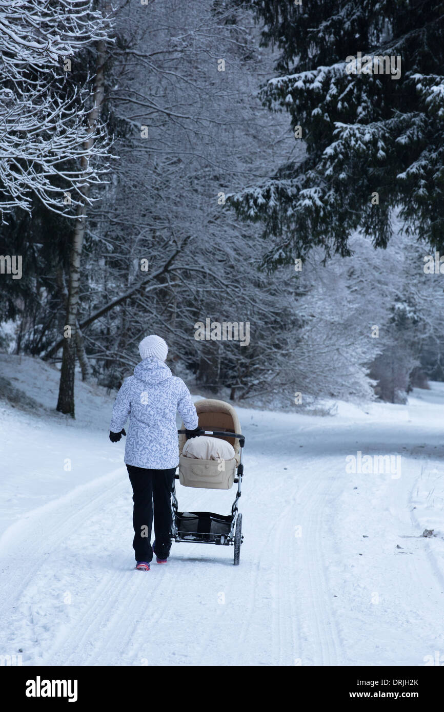 A woman pushes a pram or pushchair in a snowy forest Stock Photo