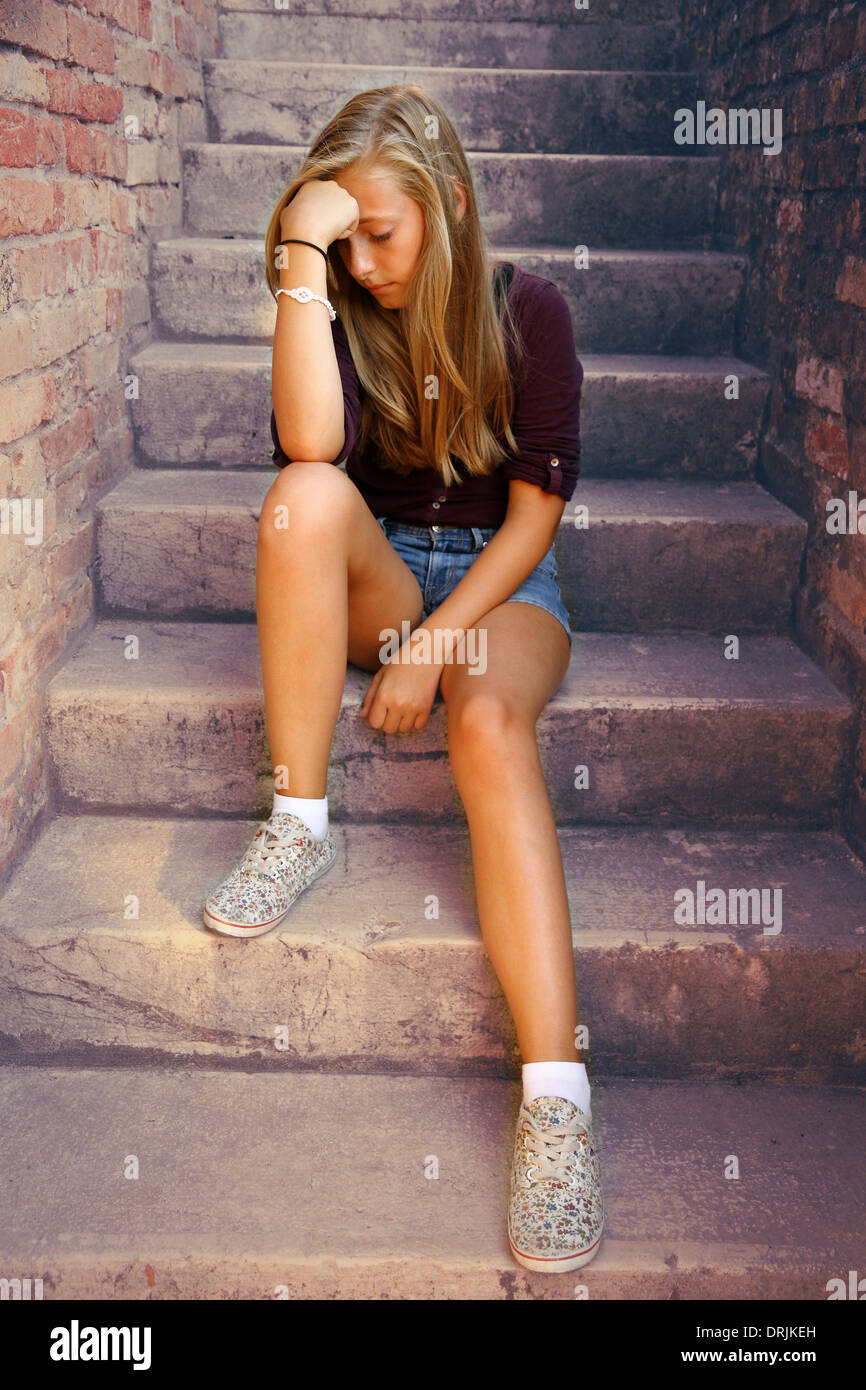 Thoughtful girl with blue eyes sitting at stone brick stairs, soft focus Stock Photo
