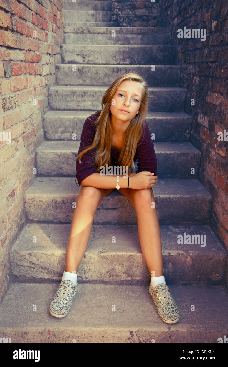 Sad girl with blue eyes sitting at stone brick stairs, soft focus Stock Photo
