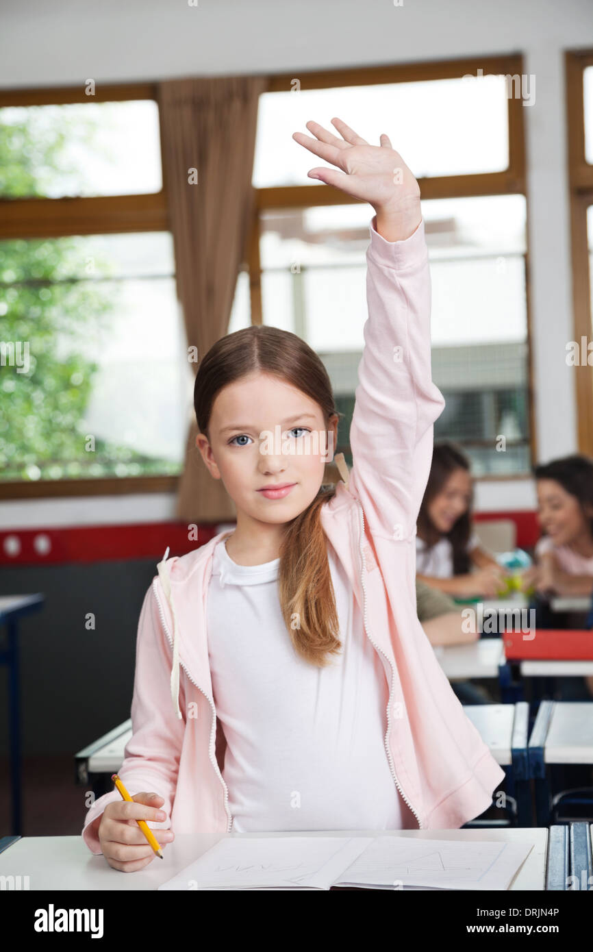 Schoolgirl Raising Hand While Standing In Classroom Stock Photo - Alamy