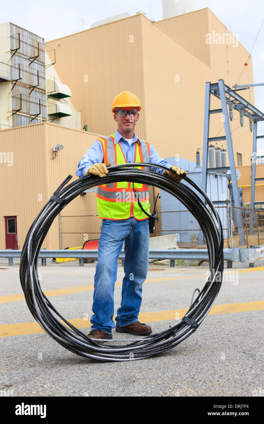 Engineer at electric power plant carrying coil of wire at storage area