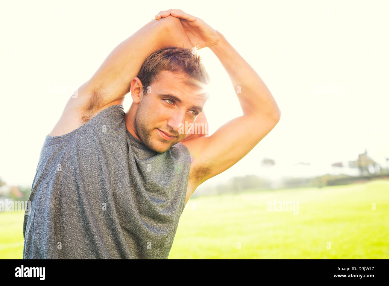 Attractive fit young man stretching before exercise workout, sunrise early morning backlit. Healthy sports fitness concept. Stock Photo