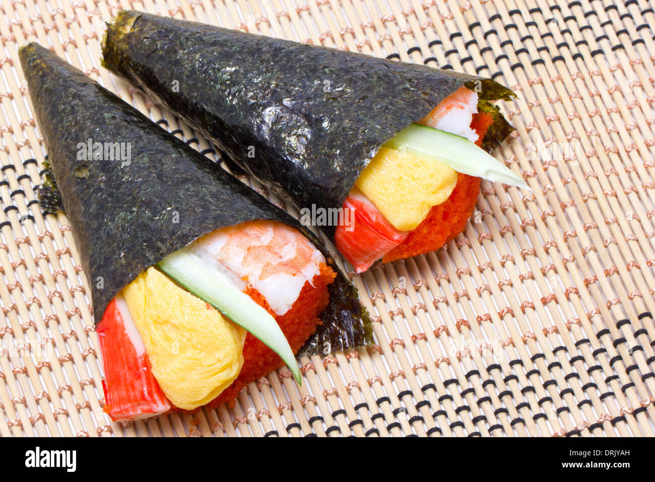Hand rolled temaki sushi traditional japanese cuisine on wooden mat. Stock Photo
