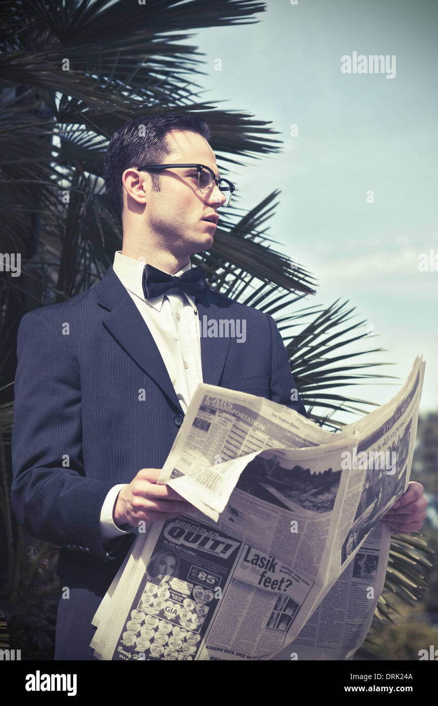 Young man in business suit and bow tie wearing 50s glasses holding newspaper looking away, an outdoor vintage style portrait Stock Photo