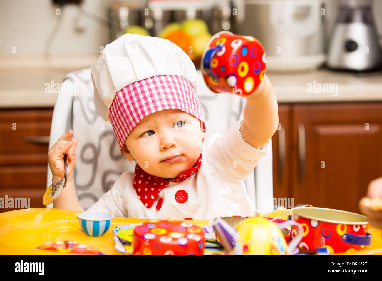 Baby cook girl wearing chef hat with utensils on kitchen. Use it for a child, healthy food
