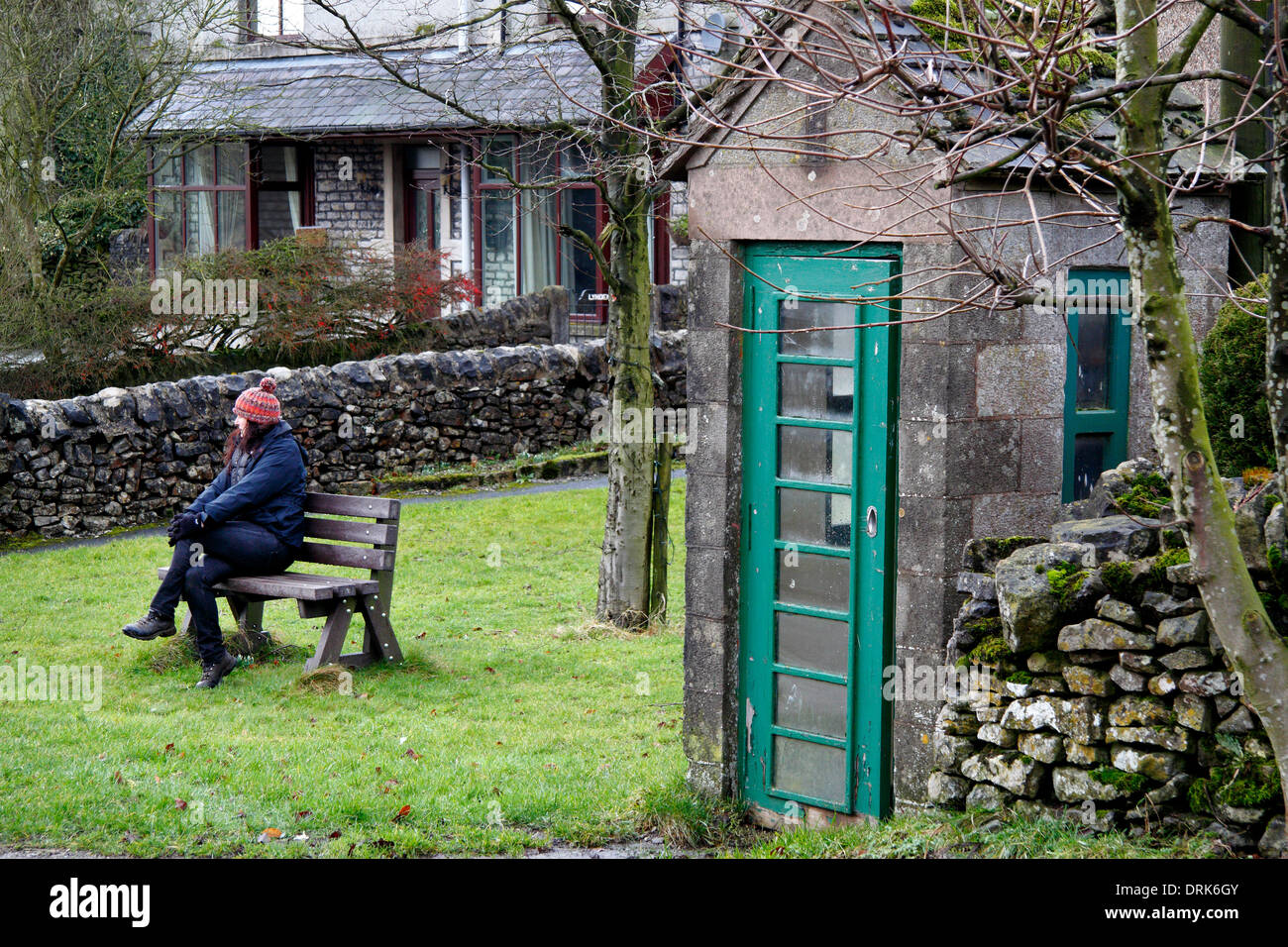 A female walker pauses by a unique green phone box built from local limestone in Chelmorton, Peak District, Derbyshire,UK Stock Photo