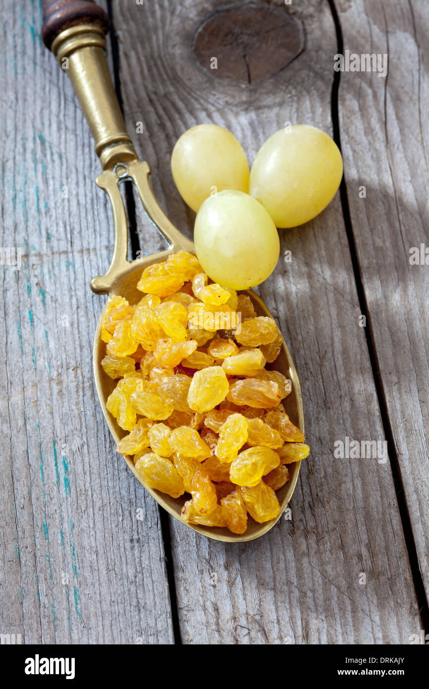Brass spoon with sultanas and three green grapes on wooden table Stock Photo