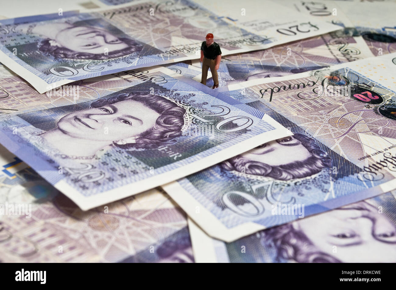 Miniature figure standing on a pile of twenty pound banknotes Stock Photo