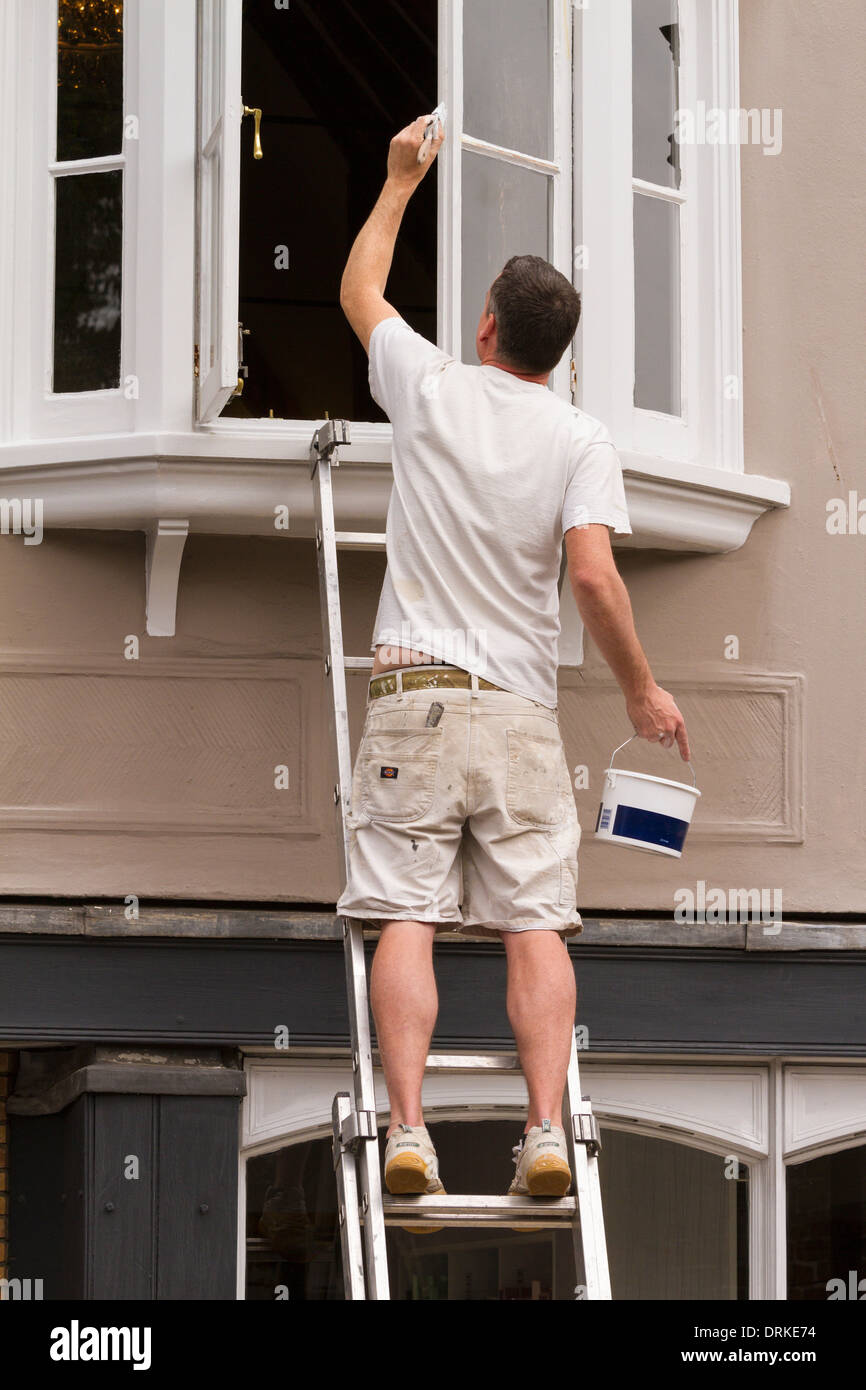 Male painter on ladder paints shop window frame white Stock Photo