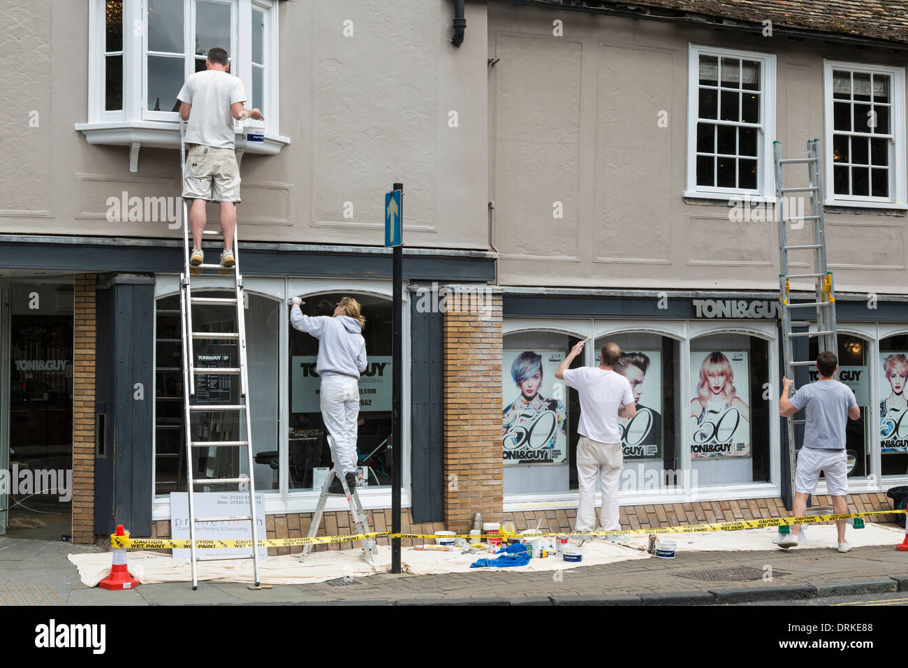 Team of painters, one on ladders, paint shop front, Cambridge, England Stock Photo