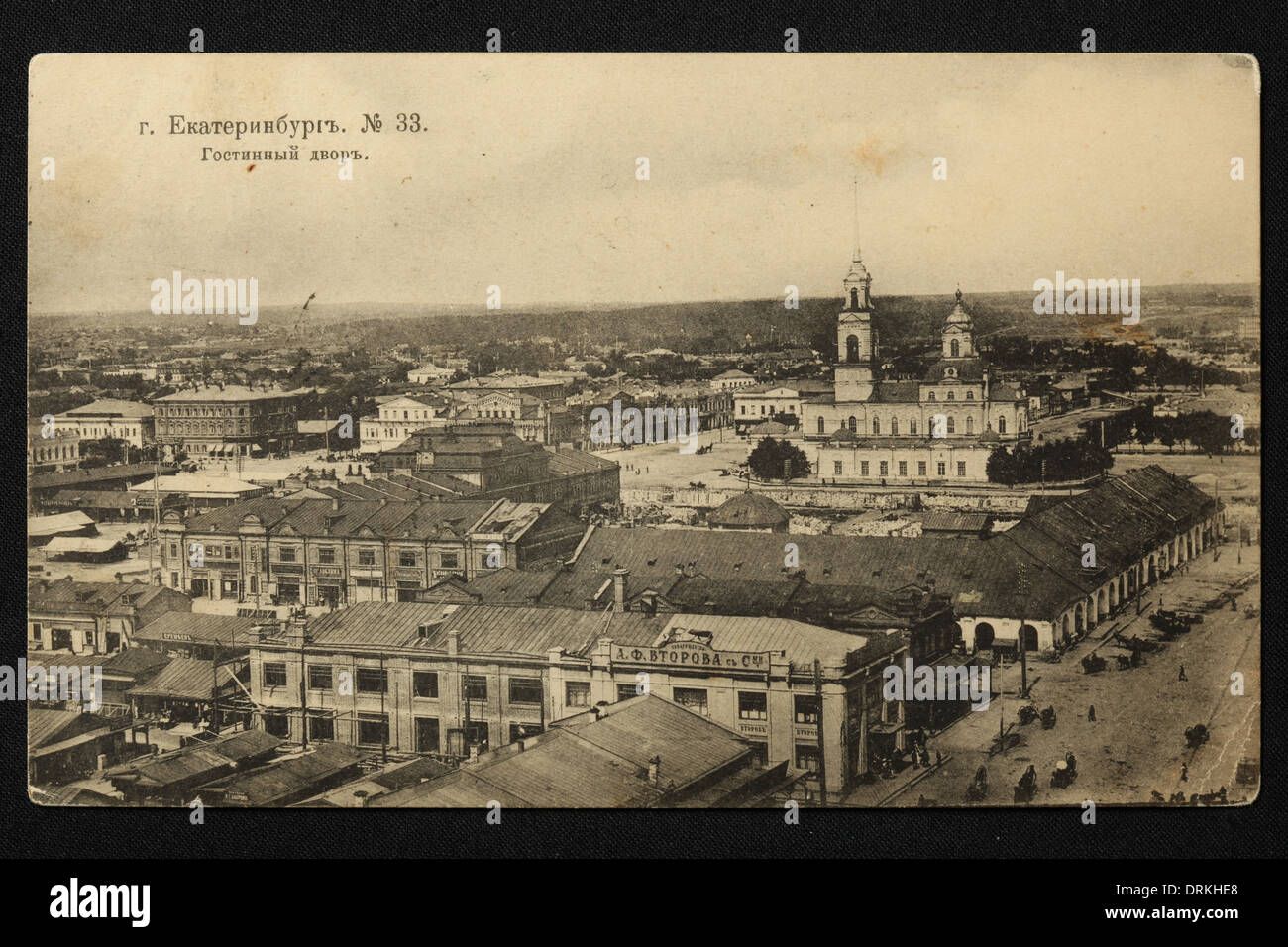 Merchant Court (Gostiny Dvor) and the Cathedral Square in Yekaterinburg, Russian Empire. Black and white vintage photograph by an unknown photographer dated from the beginning of the 20th century issued in the Russian vintage postcard published by A.S. Suvorin, Yekaterinburg. Text in Russian: Yekaterinburg. Merchant Court. View from the bell tower of the Great Zlatoust Church. The Cathedral of the Exaltation of the Cross on Cathedral Square is seen in the background. The Cathedral was demolished by the Bolsheviks in the 1930s. The Gostiny Dvor is a historic Russian term for an indoor market, o Stock Photo