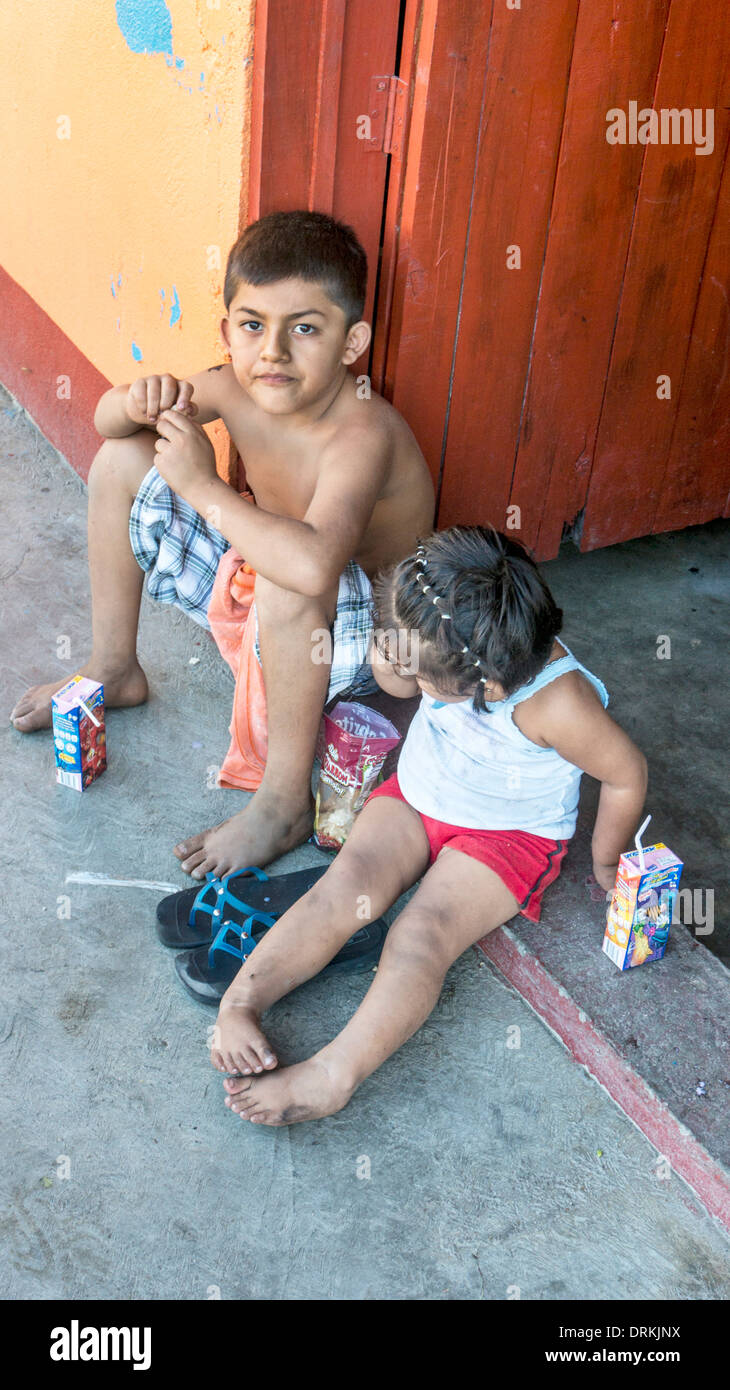 barefoot local Mexican children, small boy with defiant resigned face & his  little sister sit on door stoop with juice & chips Stock Photo - Alamy