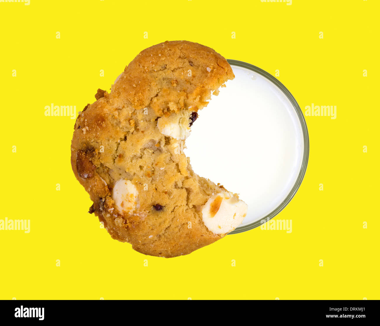 Top view of a cookie on the rim of a glass filled with skim milk on a bright yellow background. Stock Photo