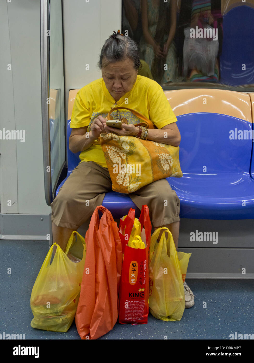 Senior Chinese woman with shopping bags in MRT train Singapore Stock