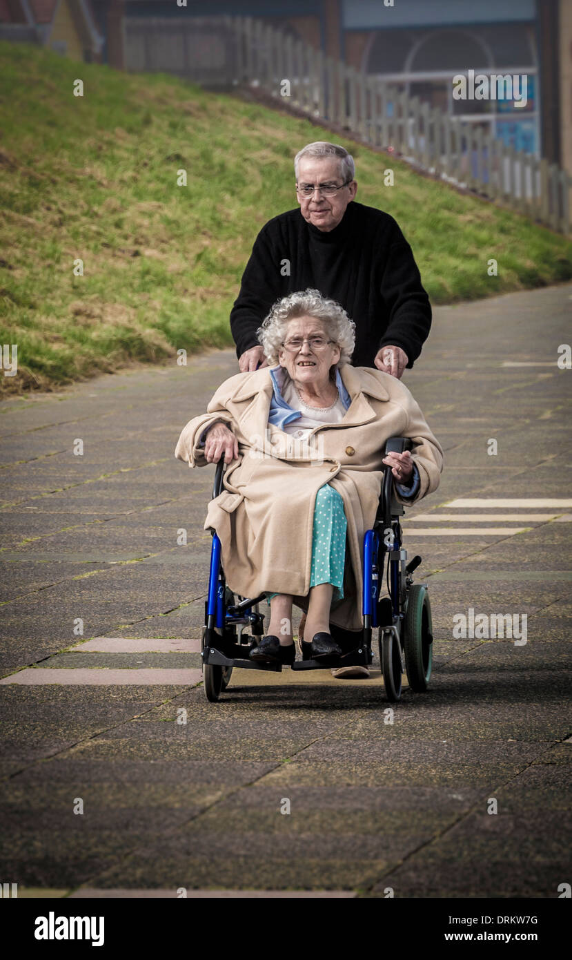 Man pushing an elderly woman in a wheelchair along the seafront at Whitley Bay, North Tyneside. Stock Photo