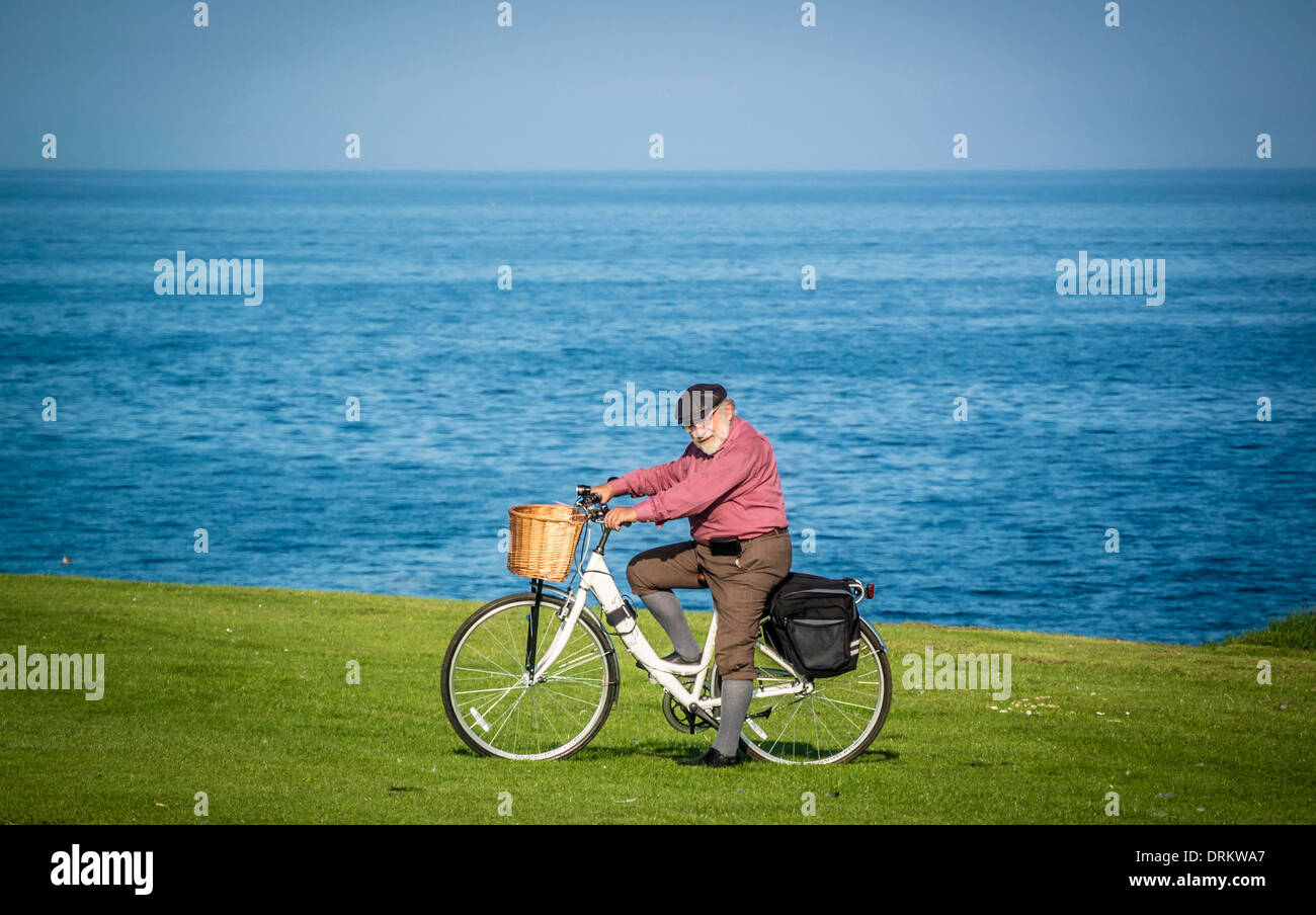 Elderly caucasian man dressed in plus four trousers on a traditional ladies bicycle, on the seafront at Whitley Bay, Tyne and Wear. Stock Photo