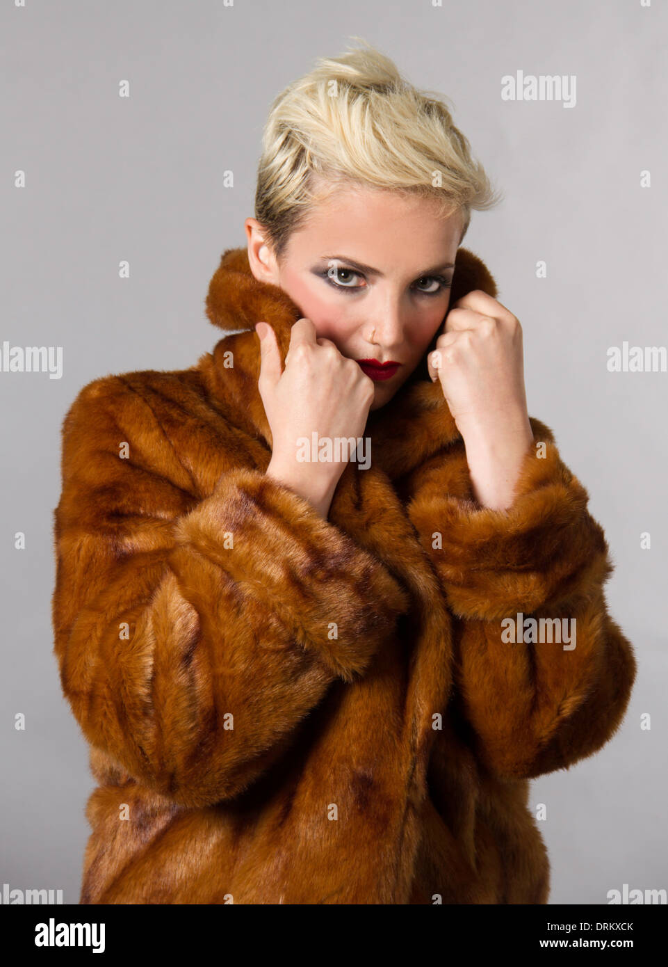 Beautiful blond model wrapped in soft brown fur coat. Hair and makeup stylist used. Many hours retouching. Stock Photo