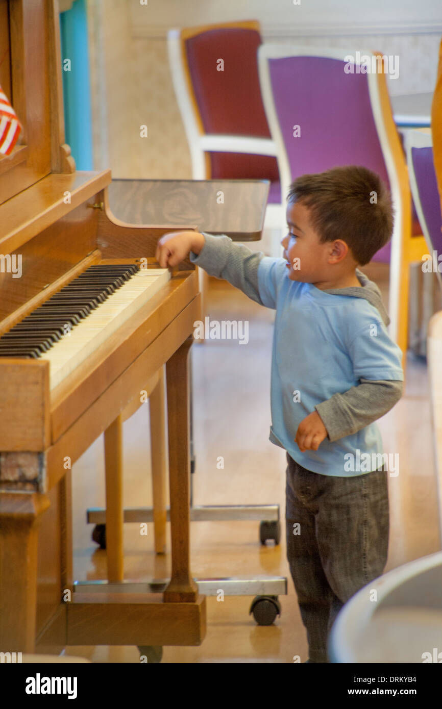 A four-year-old Asian American boy has fun trying to play a piano in Huntington Beach, CA. Stock Photo