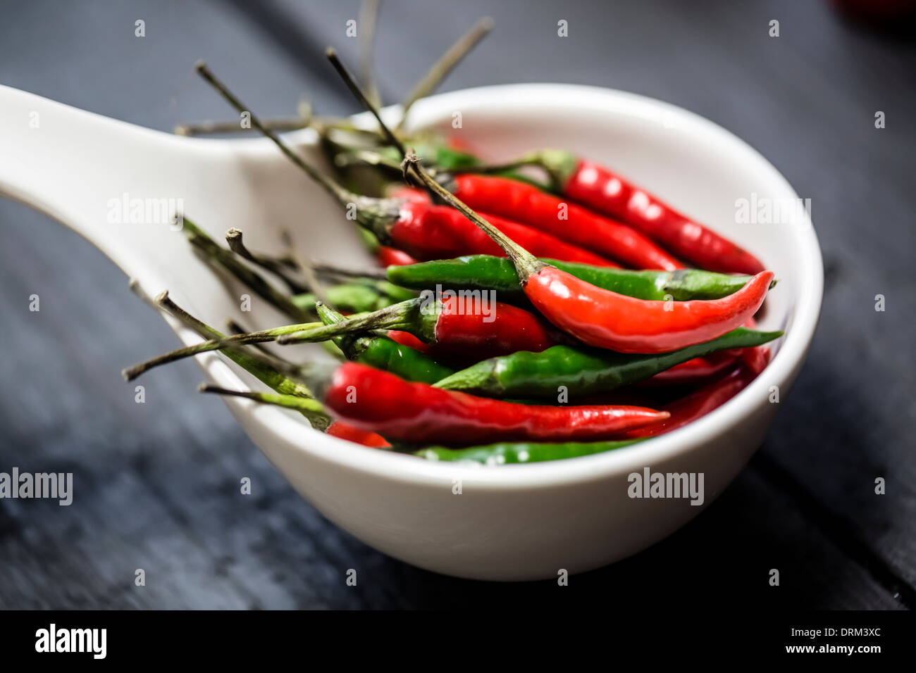 Red and green chilli peppers in a white bowl on wooden table Stock Photo
