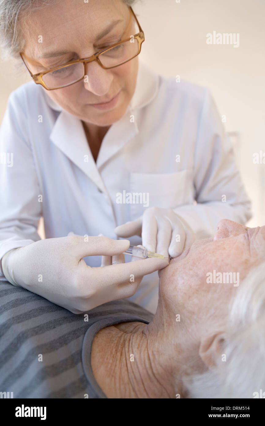 Female alternative practitioner giving senior woman injection acupuncture Stock Photo