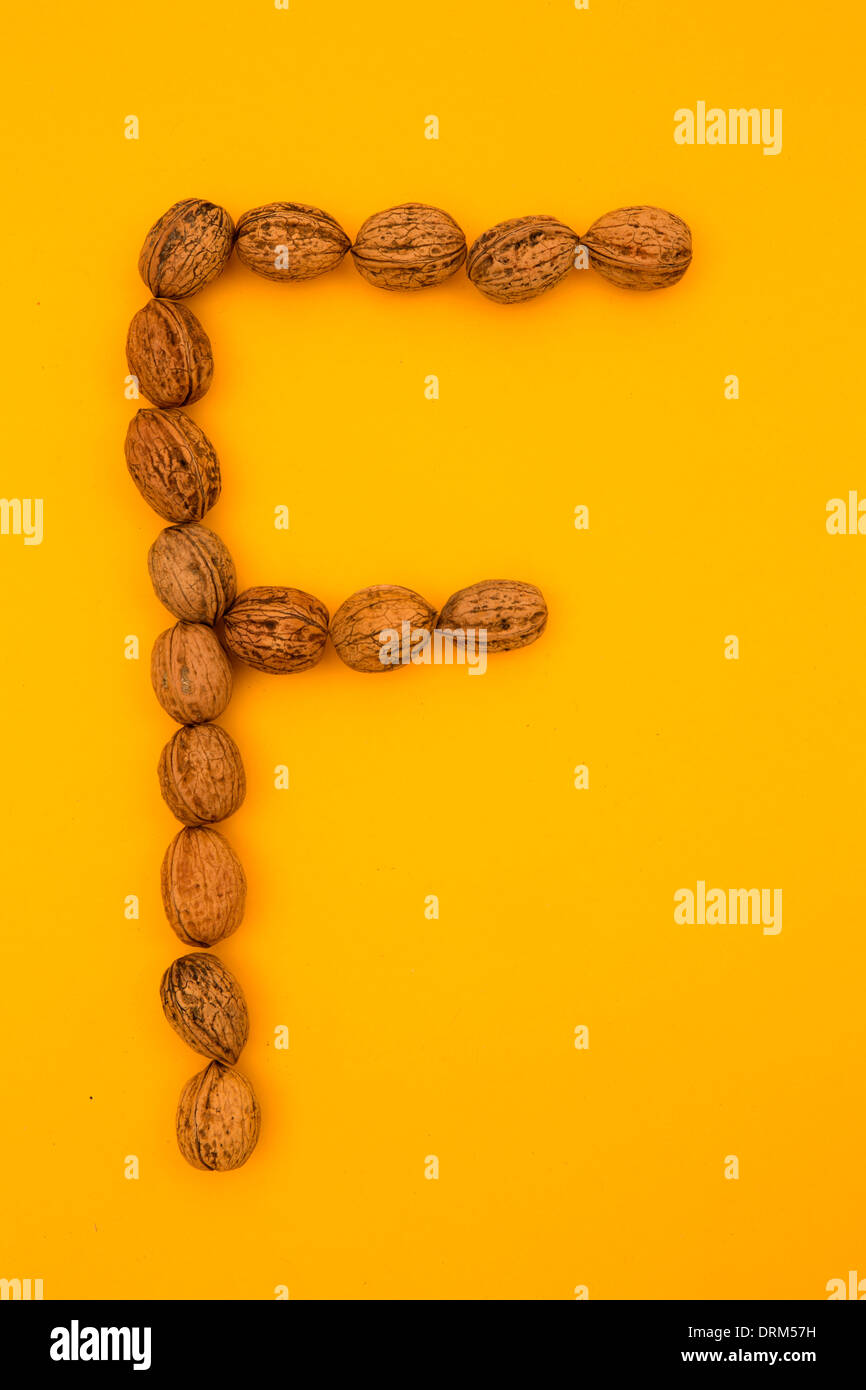 Letter 'F' formed of walnuts at yellow background, studio shot Stock Photo